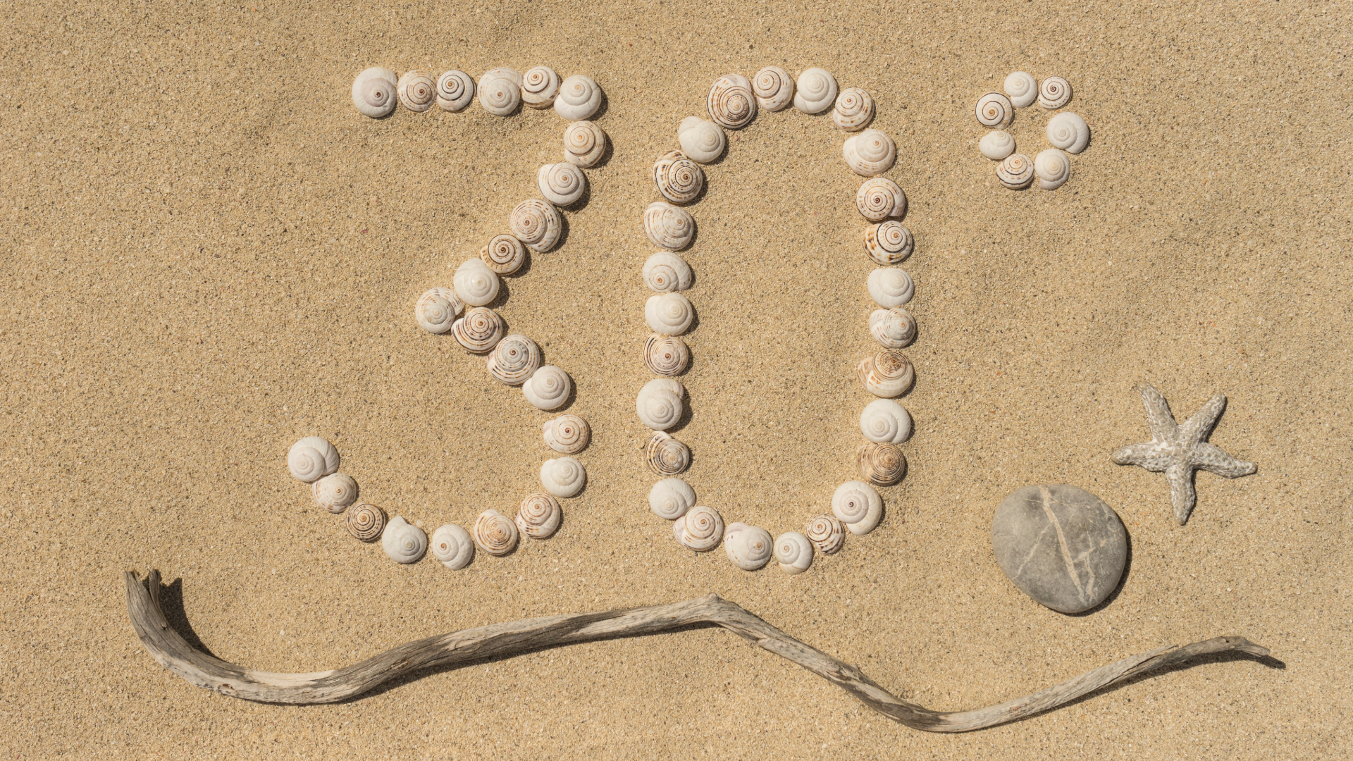 Die Zahl 30° wird mit Muscheln auf Sand, einem Treibholzstab darunter und einer Sommer-Wertkarte rechts neben einem Stein und einem Seestern gebildet.