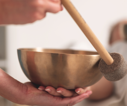 Close-up of hands holding a brass singing bowl, with one hand supporting the bowl and the other gently striking it with a padded clapper - a calming moment that combines beautifully with the invigorating cold kick according to Kneipp. Soft, blurred background.